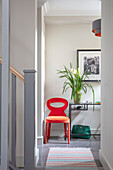 Bright red chair in hallway of Victorian cottage with striped runner London UK