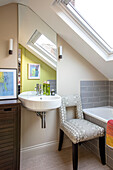 Wandbefestigtes Waschbecken und Spiegel mit Stuhl unter Dachfenster London UK