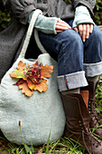 Woman sits with autumn leaf decoration on felt bag in Isle of Wight, UK