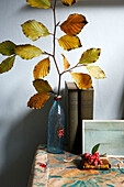 Autumn leaves in bottle on tabletop with books in Isle of Wight home UK