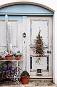 Topfpflanzen auf schmiedeeisernem Metall-Pflanzenständer an der verwitterten Eingangstür eines Hauses auf der Isle of Wight, Vereinigtes Königreich