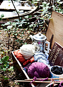 Stricken von Wolle und Brombeeren mit silberner Kaffeekanne in altem Koffer am Flussufer Isle of Wight, UK
