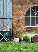 Gartengeräte an Backsteinfassade mit Bogenfenster und verwitterter Tür, Isle of Wight, UK
