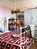 Floral baskets hang on ribbon above metal bed with crochet blanket in Isle of Wight home UK