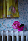 Vintage Blooms - Gelbes Blumenkleid vor zerrissener Tapete über einem Heizkörper mit einer rosa Tasse und dem Kopf einer Hortensie