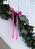 Detail of resh foliage garland on staircase with pink ribbon bow
