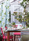 Gedeckter Ostertisch im Gewächshaus mit rosa Stühlen, Frühlingsblumen und Blumen