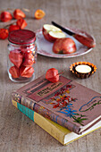 Vintage floral books with tealights cut apple on a plate and jar of chinese lantern pods
