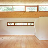 Großes modernes leeres Zimmer mit Fenstern, Holzboden und weiß gestrichenen Wänden