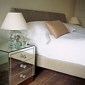 Mirrored bedside chest of drawers next to double bed in contemporary bedroom