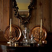 Antique silver and brass ware on tabletop with wood panelling and ornate mirror
