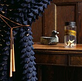 Textured fringed black curtain and copper coloured tassel in wood panelled hallway