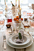 Festlich gedeckter Tisch im Esszimmer mit brennenden Kerzen und Tischset mit Teller und Serviette, gebunden mit einer Glocke und einem Tannenzweig