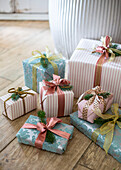 Mit Tapete verpackte und mit Bändern und Weihnachtsbaumzweigen gebundene Geschenke auf einem Holzboden unter dem Baum
