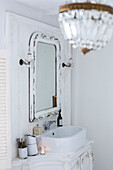 Weißes Badezimmer im skandinavischen Stil, Nahaufnahme mit kunstvoll geschnitztem Waschtisch, weißem Emaillegeschirr und hübschen Wandleuchten und Kronleuchtern aus Kristall