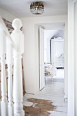 View through bedroom door to white painted mirrored wardrobe and vintage chair on painted floorboards