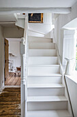 White painted staircase with shuttered window and open door leading to bedroom