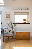 Armlehnstuhl und Holztruhe unter Fenster mit Fischdeko