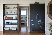Black armoire and open shelving unit, view through open door into a bedroom