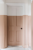 Light pink and white painted door and wall paneling in a hallway