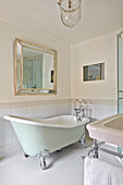 Freistehende Badewanne im antiken Stil, darüber Spiegel in hellem Badezimmer