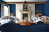 Wohnzimmer mit Kamin, blauen Sofas und Holzbalken an der Decke