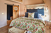 Schlafzimmer mit blumenbedruckter Bettwäsche und rustikalem Holzdekor
