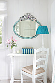 Oval mirror with floral decoration above white table and chair