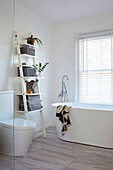 Bright bathroom with ladder shelf and free-standing tub in front of a window