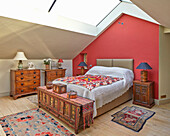 Dachgeschoss-Schlafzimmer mit roter Wand, orientalischen Teppichen und Holzmöbeln