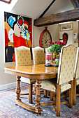 Handcrafted dining table, upholstered chairs with high backrests and modern artworks on wall in the background