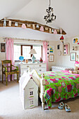 Holzbett mit bunter Decke und Puppenhäuschen im ländlichen Kinderzimmer