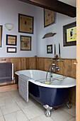 Vintage bathtub in bathroom with wooden wainscoting and old framed newspapers