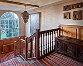 Wooden staircase banister, colorful striped carpet and old chest in the staircase in a manor house