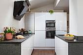 Weiße Küche mit Einbaugeräten, im Vordergrund Küchenzeile mit Granit-Arbeitsplatte