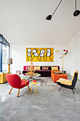 Bunte Sitzmöbel und abstrakte Kunst an weißer Wand im Wohnzimmer mit poliertem Betonboden
