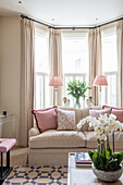 Beige sofa with throw pillows in bay window area with floor length curtains