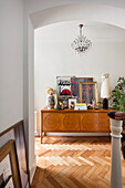 Hallway with herringbone parquet flooring and sideboard under crystal chandelier