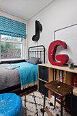 Bed with turquoise-colored blanket, large letter, music note as wall lamp and sideboard in youth room