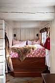 Rustic bedroom with traditional wooden bed, red patterned bed linen and fur