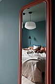 Large mirror in the bedroom with blue-grey walls and bed linen in earthy tones