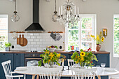 Hell gestaltete Küche mit blauer Einrichtung und Sonnenblumen auf dem Tisch