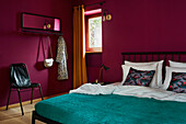 Bedroom with magenta walls, dark teal bedding and black metal bed frame