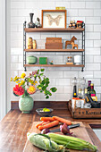 Wall shelf with decor, kitchen utensils, flowers and vegetables on worktop