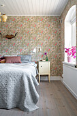 Bedroom with floral patterned wallpaper, antlers, bed and wooden floor