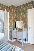 Chest of drawers with mirror in front of wall with floral wallpaper