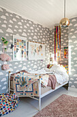 Children's room with cloud wallpaper and colourful quilt on the bed