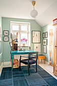 Workplace with turquoise desk and hanging lamp in a room with picture gallery