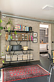 Shelf with books and magazines and red patterned carpet on floor tiles