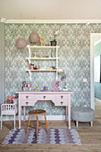 Pink desk with vintage stool in a room with floral wallpaper